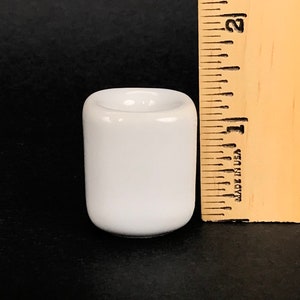 May include: A white ceramic candle holder, approximately 1 inch tall, with a round top and a smooth, glossy finish.