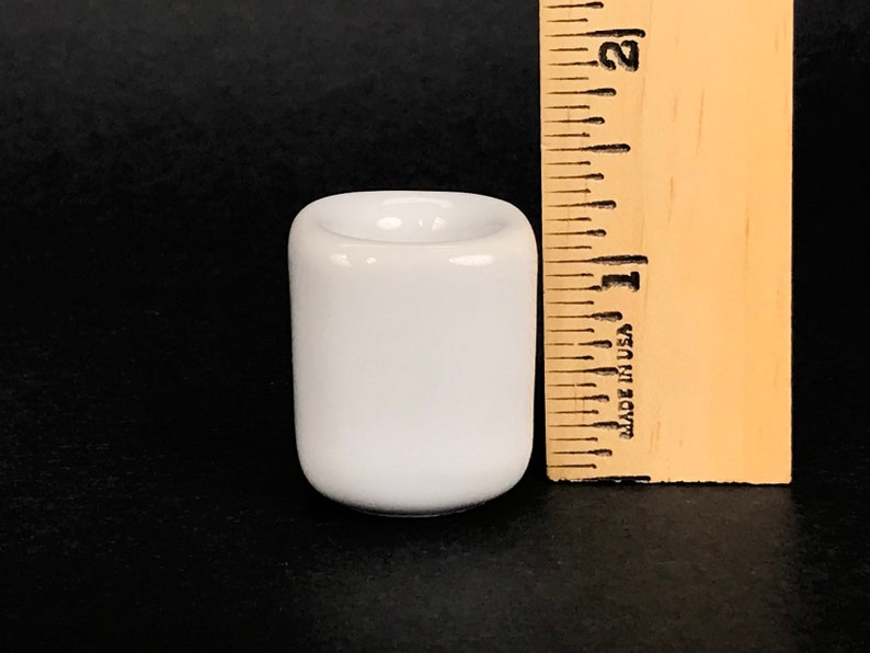 May include: A white ceramic candle holder, approximately 1 inch tall, with a round top and a smooth, glossy finish.