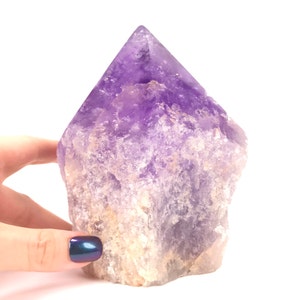 May include: A large, purple amethyst crystal point with a rough, natural texture. The crystal is approximately 15 cm tall and has a deep purple colour.