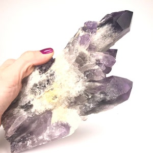 May include: A large amethyst crystal cluster with a purple and white colour scheme. The crystal has a rough, natural texture and is a beautiful example of this type of gemstone.