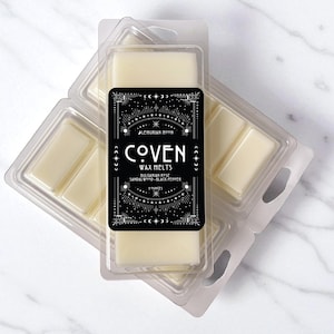 May include: Two clear plastic clamshell containers filled with off-white wax melts. A black rectangular label features the text COVEN WAX MELTS, LEMURIAN MOON, BULGARIAN ROSE, SANDALWOOD, BLACK PEPPER, and 3 OUNCES, surrounded by white celestial line art.