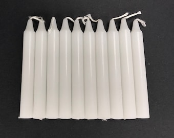 May include: A set of ten white taper candles, each approximately 6 inches long. The candles are arranged in a row on a black surface.
