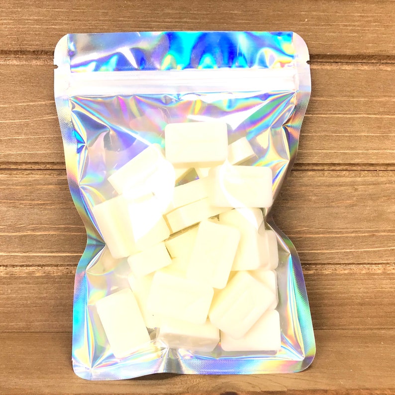 Pode incluir: Uma bolsa hologr&aacute;fica iridescente com fecho de correr, cheia de derretimentos de cera branca. A bolsa est&aacute; sobre uma superf&iacute;cie de madeira.