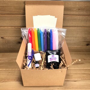 May include: A brown cardboard box filled with a crystal growing kit. The kit includes a small bag of crystals, a small bottle of liquid, a small white container, a wooden stick, a small bag of rainbow colored candles, a small bag of white candles, and a small bag of white paper.