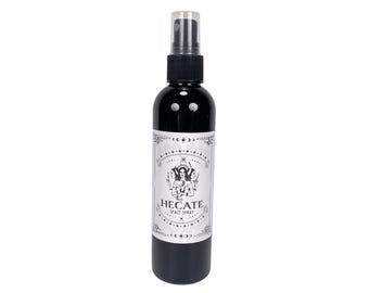 Peut inclure: Une bouteille en verre noir avec un vaporisateur noir et une étiquette blanche qui dit "Hecate Space Spray". L'étiquette présente une illustration en noir et blanc d'une femme à trois visages.