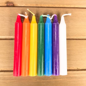 May include: Seven small, thin, coloured candles arranged in a rainbow pattern. The candles are red, orange, yellow, green, blue, purple, and white.