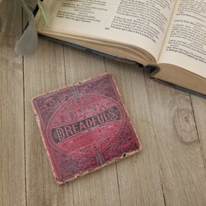 May include: A red and black square coaster with the words "The Funny Dreadfuls" printed on it. The coaster has a vintage design and is made of cork.
