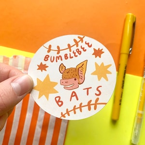 May include: A white round sticker with a brown bat illustration, the text "Bumble Bee Bats" and a yellow star design.