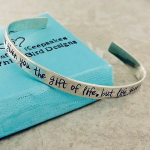 May include: Silver bangle bracelet with the inscription "You are given the gift of life, but life gives you the gift of love".