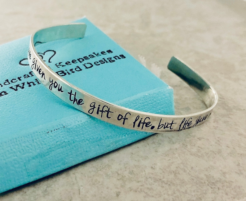May include: Silver bangle bracelet with the inscription "You are given the gift of life, but life gives you the gift of love".