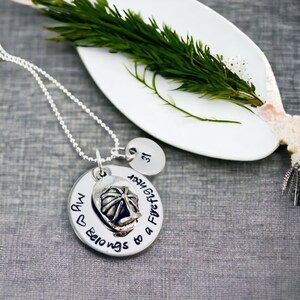 May include: A silver necklace with two charms. The larger charm is round and has the text "My ♥ Belongs to a Firefighter" with a small firefighter helmet charm. The smaller charm is round and has the number "31" on it.