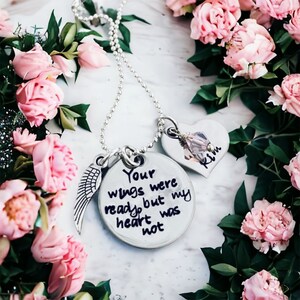 May include: Silver necklace with a heart charm engraved with the name "Kim" and a round charm with the inscription "Your wings were ready but my heart was not".