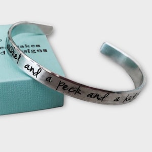 May include: A silver metal bangle bracelet with the inscription "a bushel and a peck and a hug from the neck" engraved on the band.