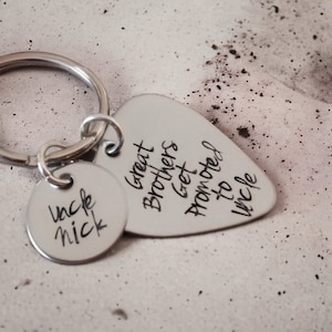 May include: Silver keychain with a guitar pick charm that reads "Great Brothers Get Promoted to Uncle" and a round charm that reads "Uncle Nick".