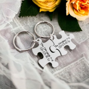 Puede incluir: Dos llaveros de plata con forma de pieza de rompecabezas con el texto "You Complete Me 02.07.15" y "You Complete Me 02.07.15" en ellos.