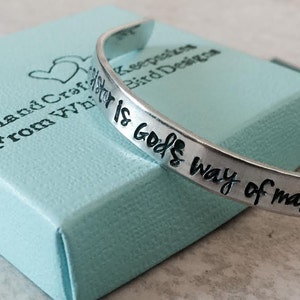 May include: Silver bracelet with the inscription "Whatever is God's way of making sure I'm okay" on a light blue box with the text "Handcrafted from wire" and two hearts.