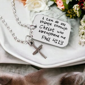 Puede incluir: Un collar de plata con un dije de cruz de plata y un dije de placa de identificaci&oacute;n de plata. La placa de identificaci&oacute;n tiene la inscripci&oacute;n "I can do all things through Christ who strengthens me Phil 4:13".