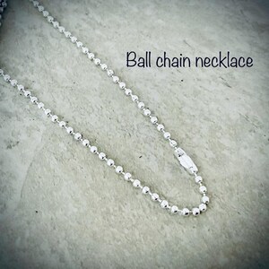 Puede incluir: Un collar de cadena de bolas plateado con cierre de broche. El collar est&aacute; sobre una superficie texturizada gris claro.  "Ball chain necklace" est&aacute; escrito en negro sobre el collar.