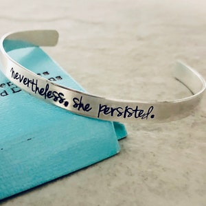 May include: Silver bracelet with the inscription "nevertheless, she persisted."