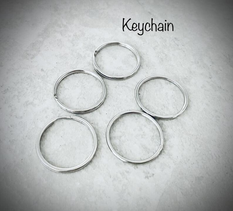 Puede incluir: Cinco llaveros plateados sobre una superficie gris. La palabra "Keychain" est&aacute; escrita sobre los llaveros.