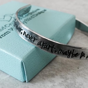 May include: A silver bracelet with the inscription "Forever, never apart, maybe in a distance" engraved on it. The bracelet is sitting on a light blue box with the words "Hand Crafted From Your Heart" printed on it.