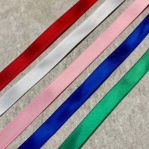 Op de afbeelding: Vijf verschillende kleuren lint, rood, wit, roze, blauw en groen, zijn diagonaal op een grijs oppervlak gerangschikt.
