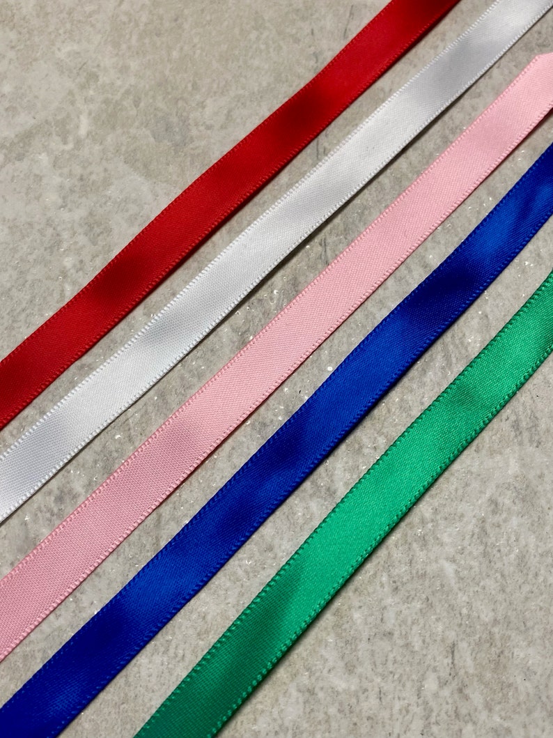 Op de afbeelding: Vijf verschillende kleuren lint, rood, wit, roze, blauw en groen, zijn diagonaal op een grijs oppervlak gerangschikt.