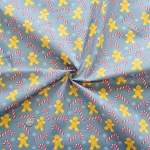 May include: A blue fabric with a repeating pattern of gingerbread men and candy canes. The gingerbread men are yellow and the candy canes are red and white.