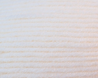 Puede incluir: Primer plano de un ovillo de lana de color crema. El hilo está bien enrollado, con crestas horizontales visibles. El color es un blanco suave y cremoso, lo que sugiere una fibra natural. Ideal para proyectos de tejido o ganchillo.
