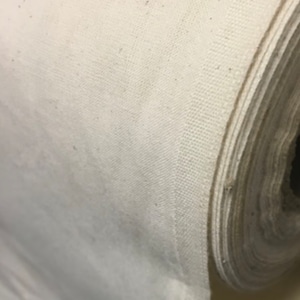 May include: Close-up of a roll of white cotton fabric. The fabric is tightly wound and has a smooth, even texture.
