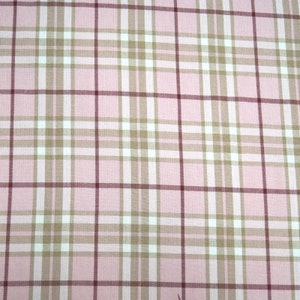 May include: Close-up of a pink plaid fabric. The pattern has a grid of white, tan, and burgundy lines over a light pink background. The fabric is likely cotton or a similar material, suitable for clothing or home decor.