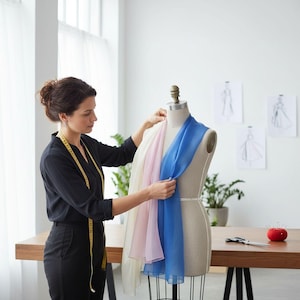 A woman in a black dress is working on a dress form, adjusting a blue scarf on it.