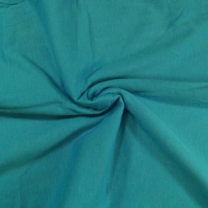 May include: A close-up of a teal blue fabric with a soft, smooth texture. The fabric is folded and draped, showcasing its draping qualities.