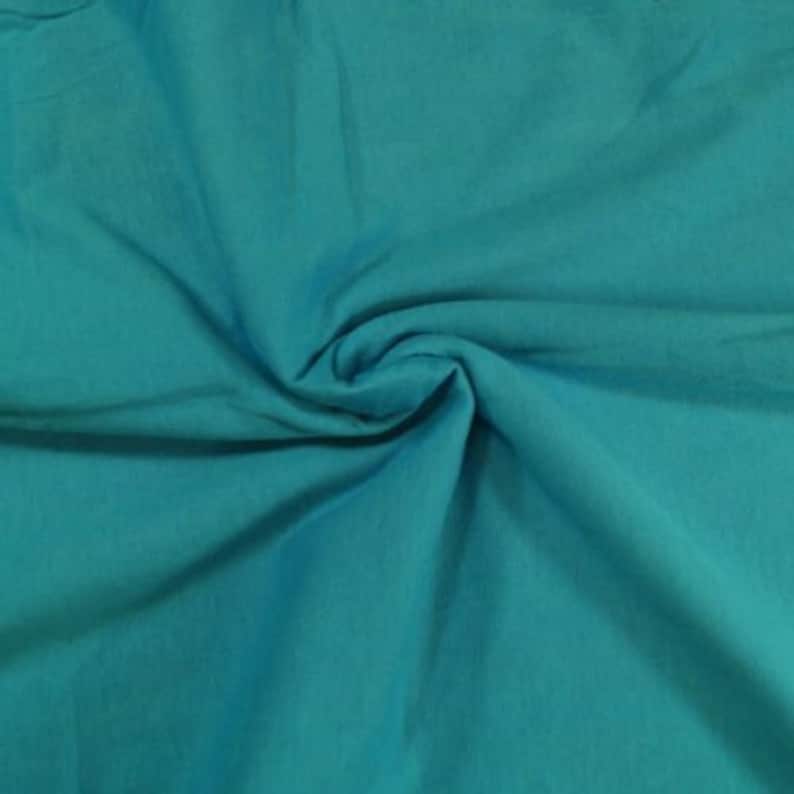 May include: A close-up of a teal blue fabric with a soft, smooth texture. The fabric is folded and draped, showcasing its draping qualities.