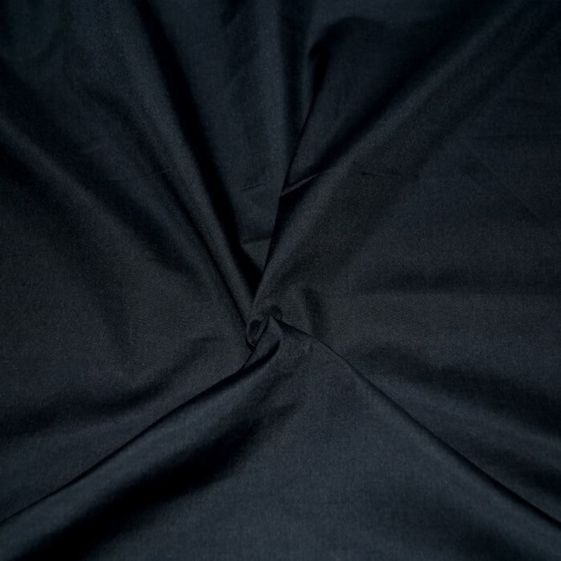 May include: A close-up of a black fabric with a smooth, silky texture. The fabric is folded and draped, creating soft folds and wrinkles.