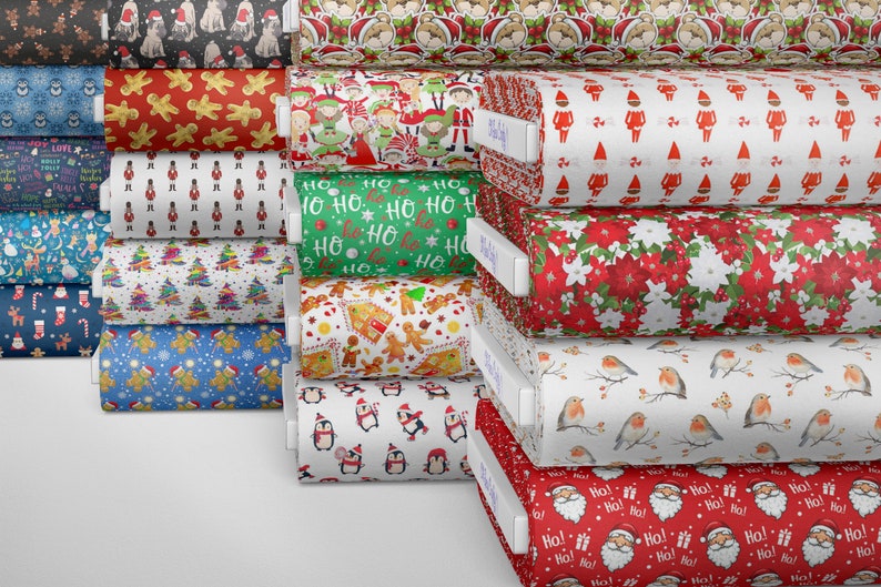 K&ouml;nnte beinhalten: Ein Stapel Stoffrollen mit verschiedenen Weihnachtsmotiven, darunter Pinguine, Lebkuchenm&auml;nner, Elfen und Weihnachtsmann. Der Stoff ist wei&szlig; mit roten, gr&uuml;nen und blauen Akzenten.