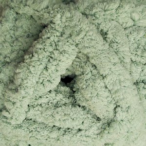 May include: Close-up of a ball of soft, textured yarn in a light green color. The yarn has a fluffy, looped texture, creating a dense and plush appearance. The center of the ball has a dark hole. Ideal for knitting and crochet projects.