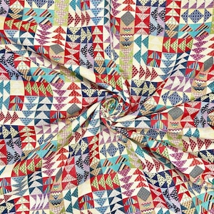 May include: A colorful fabric with a patchwork design featuring a variety of geometric shapes, primarily triangles, in shades of red, blue, green, and yellow. The fabric is folded and draped, creating a textured and visually appealing pattern.