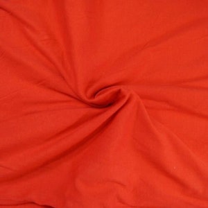 May include: A close-up of a bright red fabric with a smooth texture. The fabric is folded and draped, showing its soft and pliable nature.
