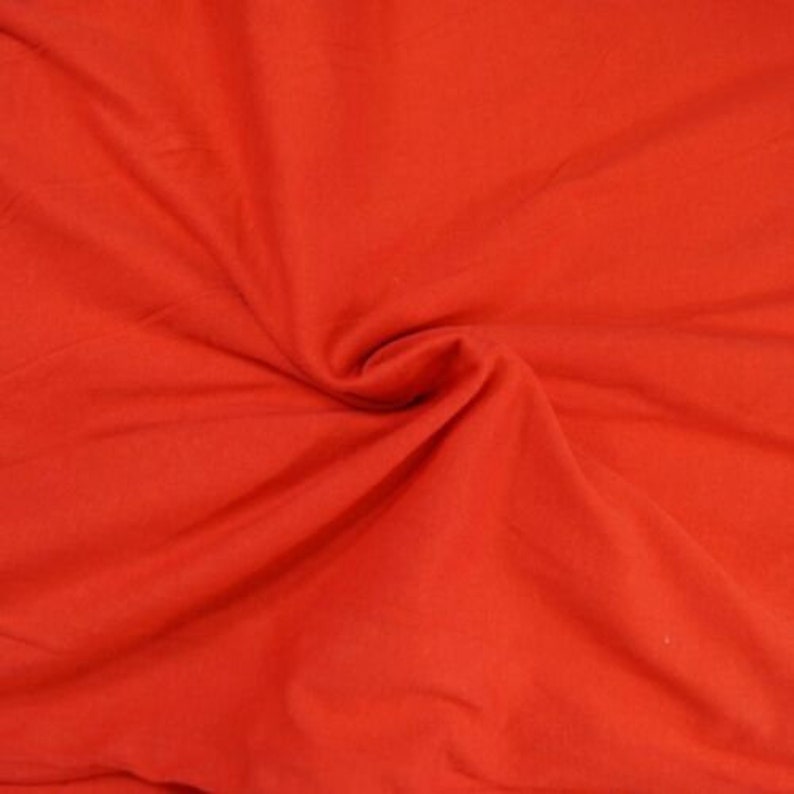May include: A close-up of a bright red fabric with a smooth texture. The fabric is folded and draped, showing its soft and pliable nature.