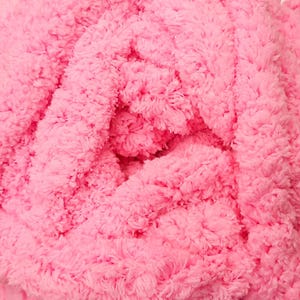 May include: Close-up of a vibrant pink, plush yarn. The yarn has a soft, fuzzy texture, with visible loops and a dense, fluffy appearance. The color is a bright, solid pink, filling the frame with its texture.