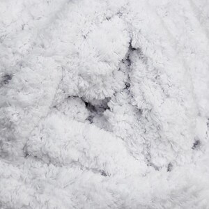 May include: Close-up of a fluffy, white, textured fabric. The material has a dense, plush appearance with a soft, cloud-like texture. The fabric's surface is uneven, with varying depths and shadows, creating a sense of depth and dimension.