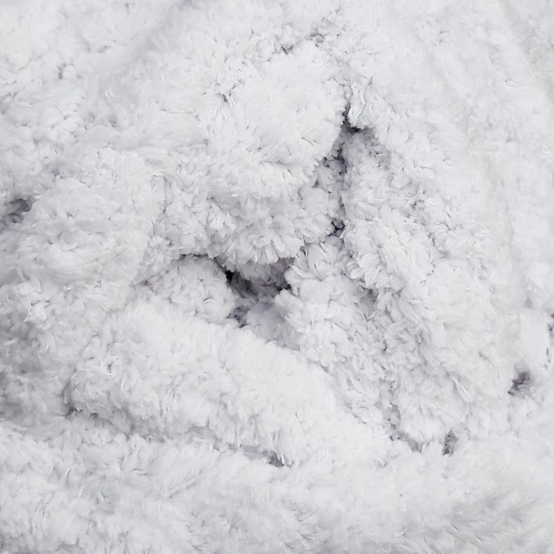 May include: Close-up of a fluffy, white, textured fabric. The material has a dense, plush appearance with a soft, cloud-like texture. The fabric's surface is uneven, with varying depths and shadows, creating a sense of depth and dimension.
