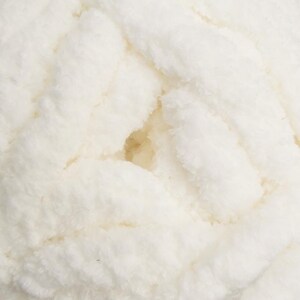 May include: Close-up of a skein of off-white, chunky yarn. The yarn has a soft, fluffy texture with visible strands and a slightly irregular surface. The color is a creamy, neutral tone, ideal for various knitting or crochet projects.