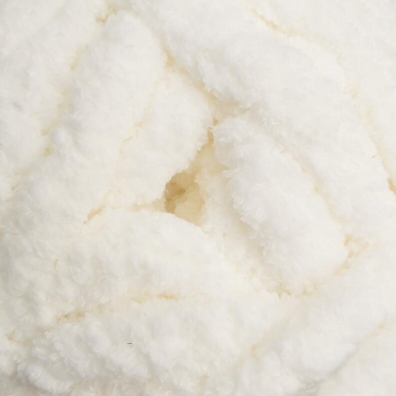 May include: Close-up of a skein of off-white, chunky yarn. The yarn has a soft, fluffy texture with visible strands and a slightly irregular surface. The color is a creamy, neutral tone, ideal for various knitting or crochet projects.
