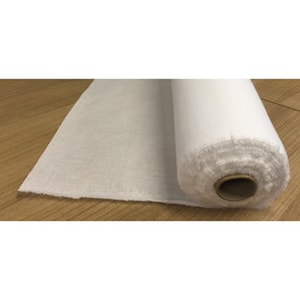 May include: A white roll of fabric, probably for quilting or crafts, is partially unrolled on a wooden surface.