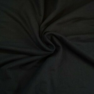 May include: A close-up of a black fabric with a soft, smooth texture. The fabric is folded and draped, creating a sense of depth and dimension.