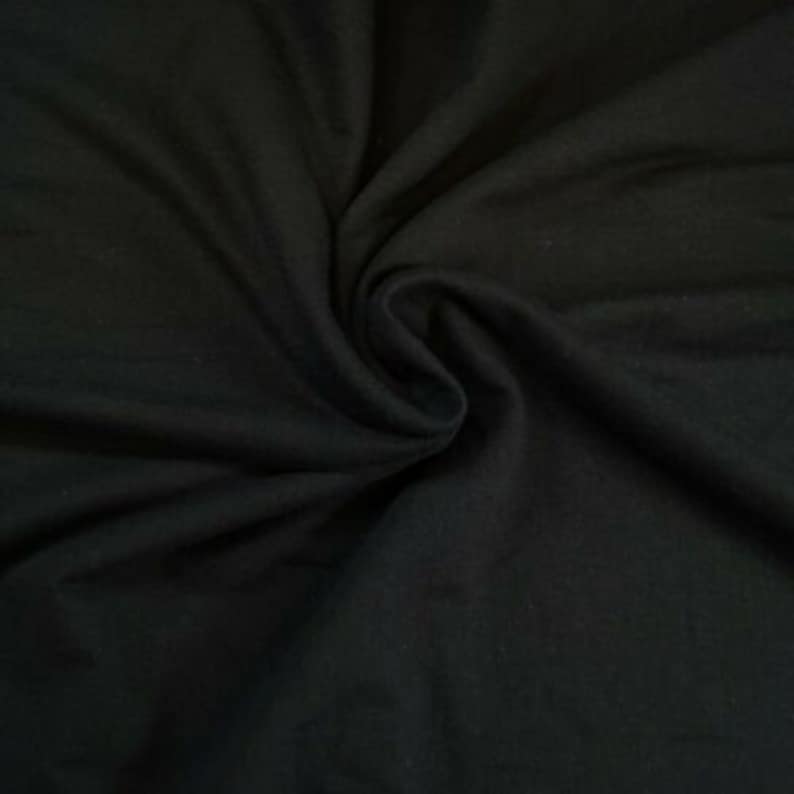 May include: A close-up of a black fabric with a soft, smooth texture. The fabric is folded and draped, creating a sense of depth and dimension.