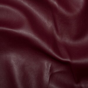 May include: Close-up of a deep burgundy faux leather fabric with a textured surface. The fabric is smooth and has a slight sheen.