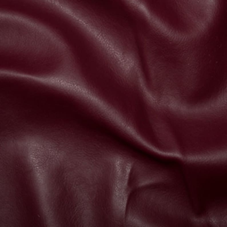 May include: Close-up of a deep burgundy faux leather fabric with a textured surface. The fabric is smooth and has a slight sheen.